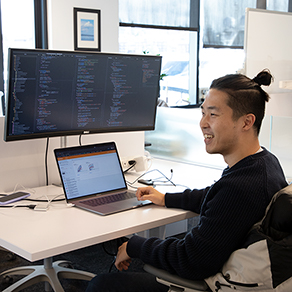 An AI2 employee smiling, sitting in front of his laptop.